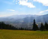 Widok z Gubałówki na Butorowy Wierch i Tatry. Słoneczny dzień, chmury na niebie.