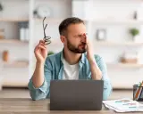 Homme fatigué, se frottant les yeux, lunettes à la main, devant son ordinateur. Il souffre de mal aux yeux à cause des écrans.