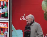 Starszy mężczyzna mija reklamę z promocją na alkohol. Włochy ceny alkoholu są atrakcyjne.