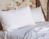 Cuscini a righe e tinta unita su un letto coperto da lenzuola di lino. Le caratteristiche del linone tessuto sono evidenti nella texture naturale.