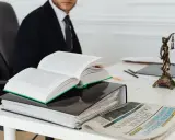Prawnik w garniturze przy biurku z książkami i aktami, gotowy do pomocy jako kurator sądowy przy rozwodzie bez orzekania o winie.