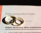 Dwa złote obrączki na odpisie skróconym aktu małżeństwa. Dokument potwierdza, ile jest ważny akt małżeństwa.