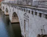Il Ponte di Tiberio a Rimini, con i suoi archi in pietra bianca che si specchiano sull'acqua scura, testimonia secoli di storia.