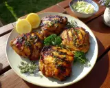 Grillade kycklinglårfileer med örter och citronklyftor, serverade på en tallrik med potatissallad i bakgrunden.