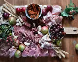 Tagliere con salumi tipici lombardi, frutta, sottaceti e grissini su un tavolo di legno.