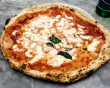 Pyszna pizza napoletana z rozpływającym się serem mozzarella i aromatycznym sosem pomidorowym, ozdobiona świeżą bazylią.