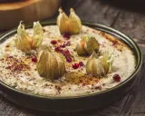 En krämig baba ganoush toppad med physalis och granatäppelkärnor på en rustik träyta.