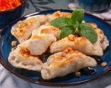 Pyszne pierogi ruskie przepis na talerzu, posypane skwarkami i udekorowane miętą.