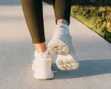 Füße in weißen Sneakern und grünen Leggings gehen auf einem Gehweg. Ein Hauch von japanischem Gehen in der Abendsonne.