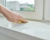 Dłoń szlifuje biały parapet, przygotowując go do montażu nakładki.