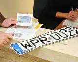 Nowe rejestracje samochodowe leżą na ladzie urzędu. Klient pokazuje dokumenty do rejestracji pojazdu.