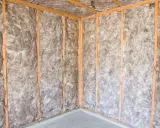 Coin d'une pièce en construction, murs et plafond recouverts d'isolation ouate de cellulose, structure en bois visible.