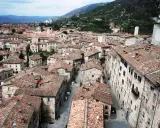 Panoramica di tetti rossi e antichi edifici in pietra, con torri medievali che svettano. Un paesaggio che ricorda l'Umbria, tra Assisi e Gubbio.