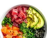 Un bol de poke coloré avec du thon, du saumon, de l'avocat et des algues, prêt à être nappé d'une délicieuse sauce poke bowl.