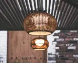 Dos lámparas de mimbre esféricas cuelgan bajo un techo de listones. La luz cálida que emiten crea un ambiente acogedor, con unos lumenes por m2 perfectos para relajarse.