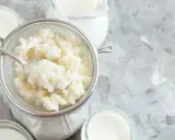 Körniger Kefir wird in einem Sieb abgetropft, bereit für die Zubereitung von Kefir-Joghurt oder einer cremigen, säuerlichen Beilage.