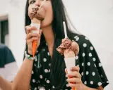 Una mujer disfruta de dos helados de chocolate, preguntándose quién inventó esta delicia.