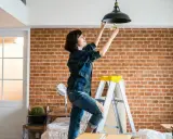 Une femme sur une échelle change une ampoule. L'indemnisation assurance obligation faire travaux est en cours.