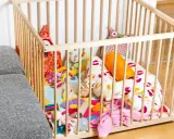Ein bunter Spielteppich mit vielen Kuscheltieren und Kissen in einem Laufstall. Ja oder nein, diese sichere Spielzone für Babys?