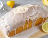 Ein saftiger Zitronenkuchen in Kastenform, überzogen mit süßem Zuckerguss. Ein Zitronenviertel liegt daneben.