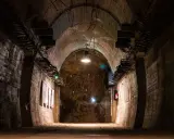 Wnętrze tunelu w Górach Sowich. Betonowe ściany, łukowe sklepienie i skalna grota z instalacją świetlną.