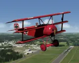 Ein rotes Fokker-Flugzeug mit Eisernem Kreuz fliegt über eine grüne Landschaft mit einer Stadt und einem Flugfeld.