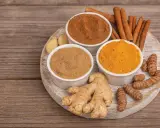 Poudre de curcuma, gingembre frais et bâtons de cannelle sur une planche en bois. Idéal pour un thé réconfortant au curcuma et miel.