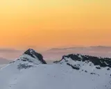 Giewont zimą o zachodzie słońca. Ośnieżone szczyty Tatr w odcieniach pomarańczy i różu.