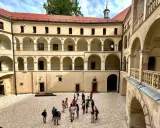 Dziedziniec zamku w Ojcowie z arkadowymi krużgankami i grupą turystów.