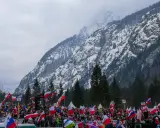 Tłum kibiców z flagami na tle ośnieżonej góry, atmosfera na skoczni w Planicy.