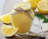 Tarro de lemon curd casero, decorado con un lazo, rodeado de limones frescos y rodajas.