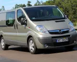 Srebrny Opel Vivaro 2.0 CDTI z przyciemnianymi szybami jedzie po drodze, otoczony zielenią.