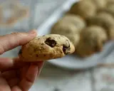 Une main tient un cookie épais et moelleux aux pépites de chocolat. D'autres cookies sont disposés sur une assiette en arrière-plan.
