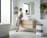 Mujer en baño moderno con deshumidificador, una solución para saber como sacar la humedad del baño sin ventilación.