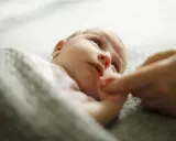 Uroczy 6 tygodniowe dziecko, otulone kocykiem, trzyma paluszek rodzica.