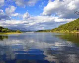 El embalse La Jarosa, con su agua serena reflejando el cielo nublado y rodeado de verdes colinas, invita a la calma.