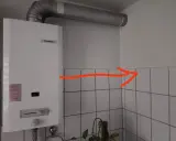 Ein Junkers-Durchlauferhitzer mit Gasflasche ist an der Wand montiert. Ein roter Pfeil zeigt auf die Ecke.