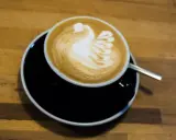Cappuccino mit Milch-Schwan-Latte-Art auf schwarzer Untertasse. Perfekt für jeden Kaffeeliebhaber.