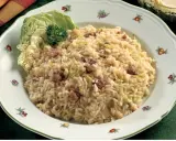 Un saporito risotto con verza e salsiccia, guarnito con una foglia di verza fresca e un ciuffo di prezzemolo.