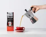 Popularna kawa Bialetti Moka wylewa się z kawiarki do czerwonej filiżanki.