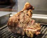 Una succulenta bistecca a Firenze, cotta alla perfezione sulla griglia, con sale grosso e fumo che sale.