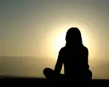 Silhuett av en person som mediterar vid solnedgången. Kanske är det en av nackdelar med meditation att man blir så fokuserad att man missar allt annat.