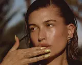 Mujer con brillos en la cara, uñas amarillas y tatuajes en la mano.