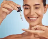 Uśmiechnięta kobieta aplikuje serum z pipetki na palec. To jej sekret na gładką skórę z retinalem 0,2.