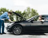 Un hombre revisa el motor de un coche negro mientras una mujer espera en el asiento del conductor. Intento arrancar el coche y no hace nada.