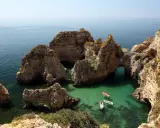 Felsformationen mit Bögen im türkisfarbenen Meer, Boote fahren vorbei. Perfektes Wetter Portugal September für einen Ausflug.