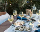 Ein gedeckter Tisch im Freien mit Austern, Brot und Gläsern voller Muscadet, einem Wein aus der Melon de Bourgogne Traube.