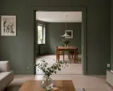Vardagsrum med soffa och ett öppet dörrhål till matsal med träbord. **Inmålade lister** ger en enhetlig känsla.