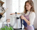 Junge Frau mit Schürze bereitet gebratenes Fleisch zum Einkochen in einem Schnellkochtopf vor.