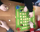 Dzieci grają w grę planszową podczas zajęć korekcyjno kompensacyjnych. Na zielonej macie są drewniane pionki i kostka.